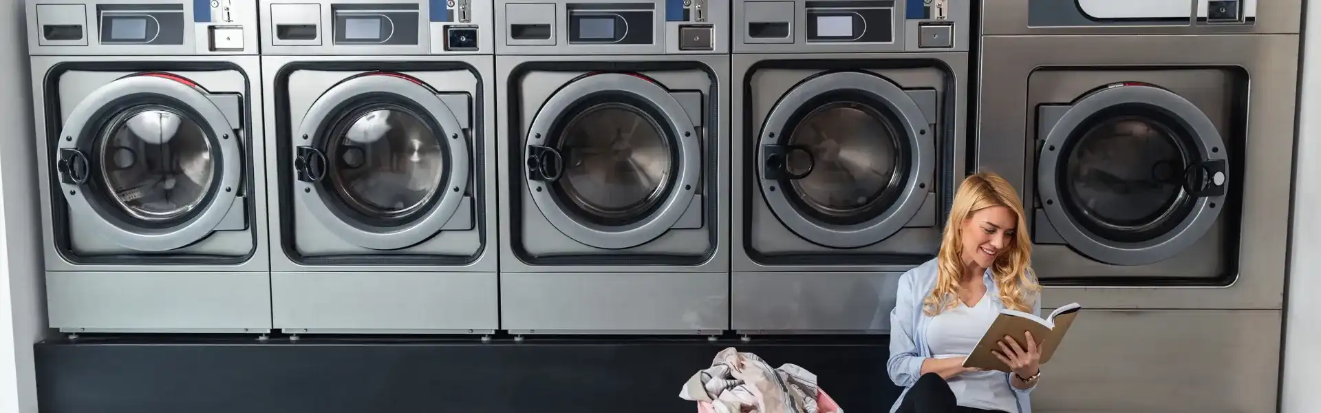 Woman Sitting On Floor Reading Book At The Laundromat 1920X600